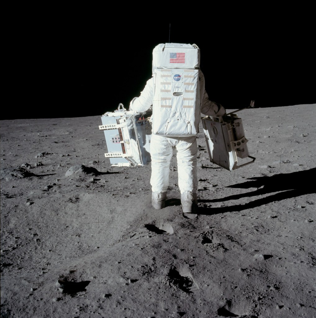 Image of Buzz Aldrin carrying the Passive Seismic Experiment Package (PSEP) in his left hand, and the Laser Ranging Retroreflector Experiment in his right hand, as he head into position for deployment. Taken by Neil Armstrong on the moon, July 20th 1969. (Image courtesy: NASA)