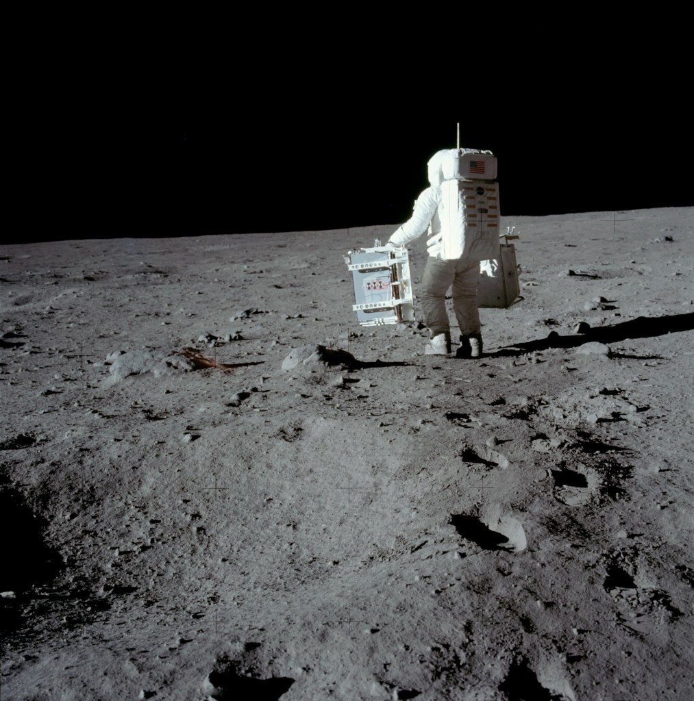 Image of Buzz Aldrin carrying the Passive Seismic Experiment Package (PSEP) in his left hand, and the Laser Ranging Retroreflector Experiment in his right hand, as he head into position for deployment. Taken by Neil Armstrong on the moon, July 20th 1969. (Image courtesy: NASA)